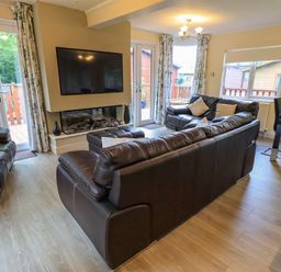 A living room with brown leather sofas a mounted TV and two sets of glass doors at Thirlmere View Thirlmere 6 White Cross Bay near Windermere