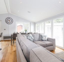 A living area with grey sofas, bar stools, a dining table, and large windows at Lakes Lodge Keswick Court 3 White Cross Bay near Windermere
