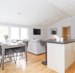 An open plan kitchen and dining area with a dining table set for six and a kitchen island with bar stools at Lakes Lodge Keswick Court 3 White Cross Bay near Windermere