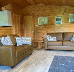 A living room with two brown leather sofas and plaid pillows wooden walls and framed maps at Glaramara Number 7 Burnside Park near Keswick