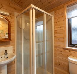 A bathroom with a shower cubicle a sink with taps a mirror and a window at Rivendell Burnside Park Number 14 Burnside Park near Keswick