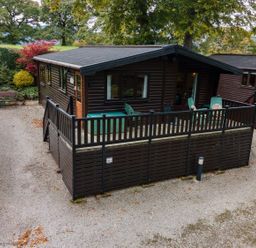 A small wooden cabin with a fenced porch and green chairs at Rivendell Burnside Park Number 14 Burnside Park near Keswick
