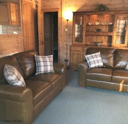 A living room with two brown leather sofas and wooden cabinets at Rivendell Burnside Park Number 14 Burnside Park near Keswick