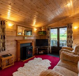 A living room with wooden walls and ceiling a fireplace a television sofas and sliding doors leading outside at Burr Ghyll Number 27 Burnside Park near Keswick