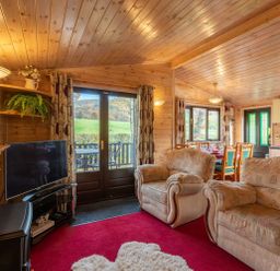A living room with armchairs a television and dining table in a wooden cabin at Burr Ghyll Number 27 Burnside Park near Keswick