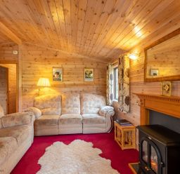 A living room with wooden walls and ceiling sofas a lamp a fireplace and a rug at Burr Ghyll Number 27 Burnside Park near Keswick