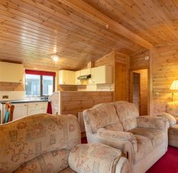 A living room with patterned sofas a kitchen area with white cabinets and a dining table with red tablecloth at Burr Ghyll Number 27 Burnside Park near Keswick