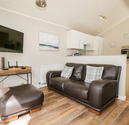 A living room with a brown leather sofa and ottoman a wall-mounted tv and a wooden cabinet at Troutbeck Lodge Beckside 6 Limefitt Park near Windermere