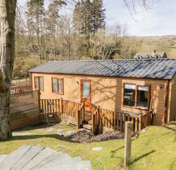 An exterior view of a wooden lodge with a small fenced porch and steps leading to the door surrounded by grass and trees at Troutbeck Lodge Beckside 6 Limefitt Park near Windermere
