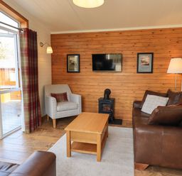 A living room with a brown leather sofa a grey armchair a wooden coffee table and a wall-mounted TV at Ramblers Rest Lodge Pinewood 22 Limefitt Park near Windermere