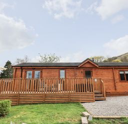 A wooden cabin with a fenced deck and patio umbrella on grass and gravel at Ramblers Rest Lodge Pinewood 22 Limefitt Park near Windermere