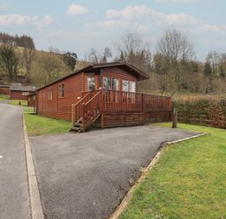 A wooden lodge with a small deck and stairs beside a paved driveway surrounded by grass at Striding Edge Lodge Ullswater 9 Limefitt Park near Windermere