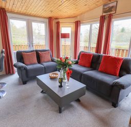 A living room with two grey sofas and a coffee table with flowers at Striding Edge Lodge Ullswater 9 Limefitt Park near Windermere