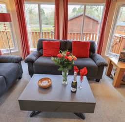 A living room with two gray sofas with red cushions and a gray coffee table with flowers and a bottle at Striding Edge Lodge Ullswater 9 Limefitt Park near Windermere