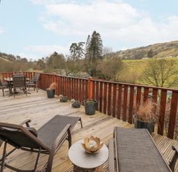 A wooden deck with lounge chairs a table with chairs and potted plants overlooking hills and trees at Horseshoe Lodge Wansfell 5 Limefitt Park near Windermere