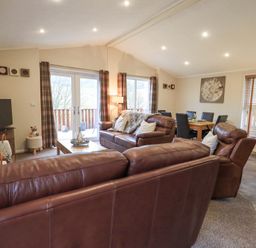 A living room with brown leather sofas a coffee table a dining table with chairs and large windows at Horseshoe Lodge Wansfell 5 Limefitt Park near Windermere