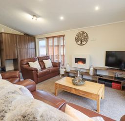 A living room with brown leather sofas a wooden coffee table a wall-mounted electric fireplace a flat-screen TV on a wooden stand and decorative wall art at Horseshoe Lodge Wansfell 5 Limefitt Park near Windermere
