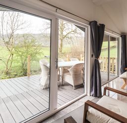 A dining area with sliding glass doors opening to a deck with outdoor chairs and table at Jinnyspinner Lodge Beckside 37 Limefitt Park near Windermere