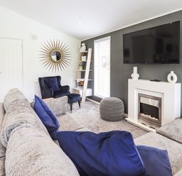 A living room with a gray sofa and blue cushions a black armchair a fireplace a wall-mounted television and a decorative mirror at Jinnyspinner Lodge Beckside 37 Limefitt Park near Windermere