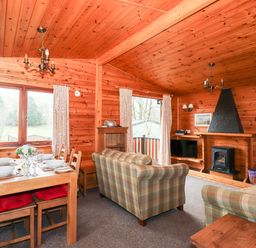 A living room with a dining table set for six people and two plaid sofas next to a fireplace at Rowan Lodge in Pinewood 16 Limefitt Park near Windermere
