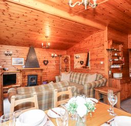 A wooden living room with plaid sofas a dining table set with plates and glasses a TV and a stove at Rowan Lodge Pinewood 16 Limefitt Park near Windermere