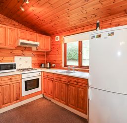 A kitchen with wooden cabinets a white oven microwave refrigerator and sink at Rowan Lodge Pinewood 16 Limefitt Park near Windermere