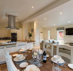 A dining table set with plates glasses and a bottle of wine in an open plan kitchen and living area at Langdale Lodge Langdale 21 White Cross Bay near Windermere