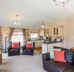 A living room with brown leather chairs and a sofa with cushions near a kitchen with light wood cabinets at Hideaway Lodge Kirkstone 14 Limefitt Park near Windermere
