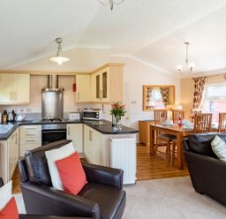 An open kitchen with cream cabinets a dining table set with chairs and a living area with leather sofas at Hideaway Lodge Kirkstone 14 Limefitt Park near Windermere