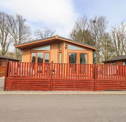 A wooden cabin with a red wooden fence in front surrounded by leafless trees at Valley View Lodge Wansfell 10 Limefitt Park near Windermere