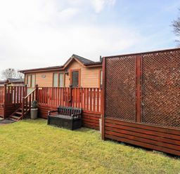 An outdoor view of a wooden lodge with railing and steps a bench and lattice fences at Valley View Lodge in Wansfell 10 Limefitt Park near Windermere