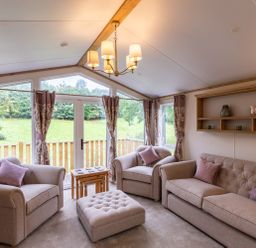 A living room with beige sofas a wooden coffee table and large windows with curtains at Latterbarrow Lodge in Beckside 46 Limefitt Park near Windermere