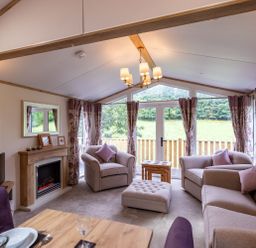 A living room with armchairs a sofa an ottoman fireplace and large windows at Latterbarrow Lodge Beckside 46 Limefitt Park near Windermere