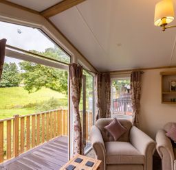 A sitting area with armchairs and a wooden balcony overlooking a green field at Latterbarrow Lodge Beckside 46 Limefitt Park near Windermere