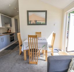 A dining area with wooden chairs and a table beside a kitchen and glass door at Robin View Lodge Beckside 3 Limefitt Park near Windermere