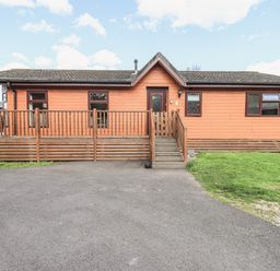 An exterior view of a single-story wooden lodge with a small porch and steps leading to the front door at Sunny Brow Lodge Lakeside 5 White Cross Bay near Windermere