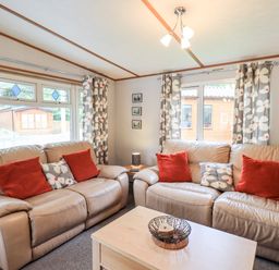 A living room with two beige leather sofas with orange and floral cushions a wooden coffee table and floral curtains at Pinehaven Lodge Grasmere 6 White Cross Bay near Windermere