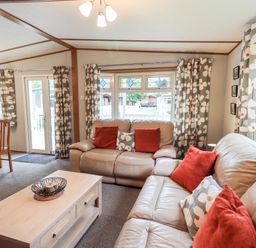 A living room with leather sofas and a wooden coffee table near windows with floral curtains at Pinehaven Lodge Grasmere 6 White Cross Bay near Windermere