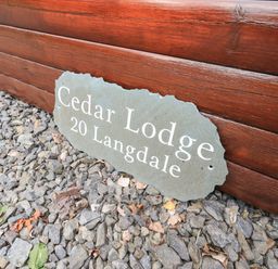 A sign reading Cedar Lodge 20 Langdale on gravel next to a wooden log wall at Cedar Lodge Langdale 20 White Cross Bay near Windermere