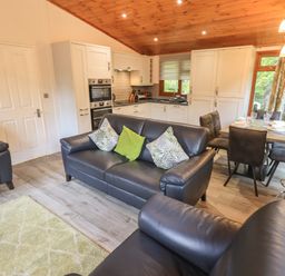 An open living area with black leather sofas and green cushions a dining table with chairs and white kitchen cabinets at Cedar Lodge Langdale 20 White Cross Bay near Windermere