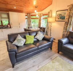 A living area with black leather sofas and a kitchen with white cabinets at Cedar Lodge Langdale 20 White Cross Bay near Windermere