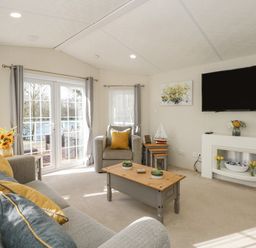 A living room with a sofa, armchair, coffee table, TV, fireplace, and flowers at Lakeside View in Pentney near King's Lynn
