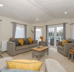 A living room with sofas, a coffee table, side tables, curtains, and glass doors at Lakeside View in Pentney near Kings Lynn
