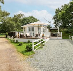 A gravel driveway leading to a white mobile home with porches and an umbrella at Lakeside View in Pentney near Kings Lynn