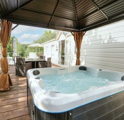 An outdoor wooden deck with a hot tub under a canopy and a dining table with chairs at Lakeside View in Pentney near King's Lynn