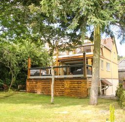 A wooden deck with outdoor furniture attached to a yellow house with trees and grass around Sunnyside Bircher Common near Yarpole
