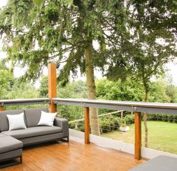 A wooden deck with gray outdoor seating and white pillows overlooking a garden with trees at Sunnyside Bircher Common near Yarpole