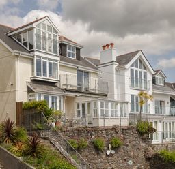 A row of multi-story houses with balconies and large windows overlooking a stone wall with plants at Seascape in Salcombe