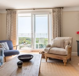 A living room with chairs a wooden coffee table a bookshelf and a balcony door at Seascape in Salcombe