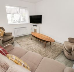 A living room with a sofa and armchairs around a wooden coffee table and a wall-mounted television at Trigfa in Llanfechell